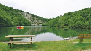 Eine friedliche Uferlandschaft mit Picknicktisch und Bänken, umgeben von üppiger Vegetation und einer steinigen Klippe.