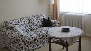 A living room with a patterned sofa, a small round table with a bowl, a lamp, and a radiator. - Apartment Hannah (Neubrandenburg)