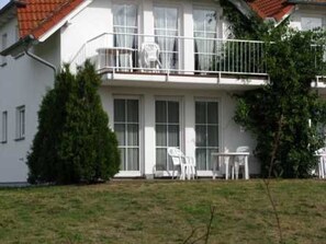 Ein zweistöckiges Gebäude mit Balkon, einem kleinen Garten und Gartenmöbeln.