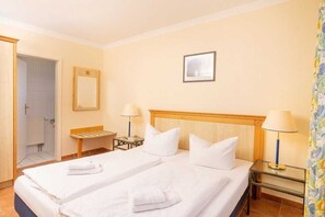 Ein Hotelzimmer mit zwei Betten, einem Holzkopfende, zwei Nachttischlampen, einem kleinen Tisch und einem durch eine geöffnete Tür einsehbaren Badezimmer.