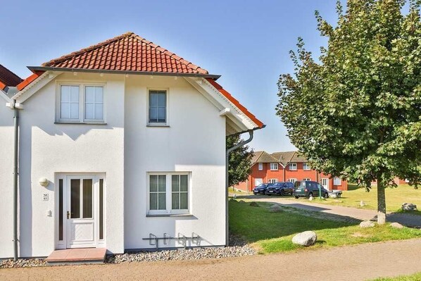 Ein zweistöckiges Wohnhaus mit rotem Ziegeldach, weißen Außenwänden und einer kleinen Veranda.