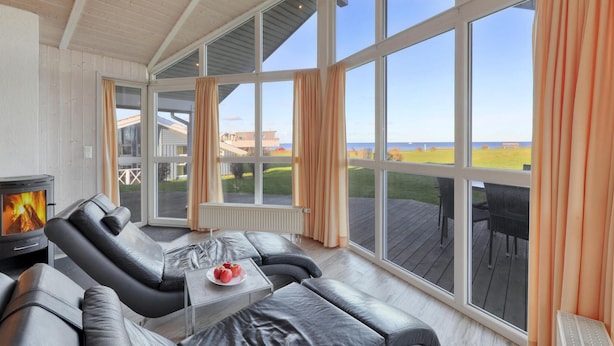 A modern living room with a fireplace, leather sofas, and large windows offering a view of the outdoors. - Amazing home in Schönhagen with sauna (Schönhagen)