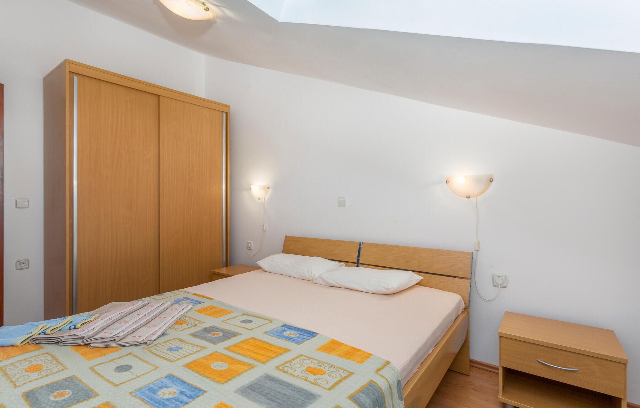 Ein Schlafzimmer mit Bett, Holzschrank, Nachttisch und zwei Wandleuchten.