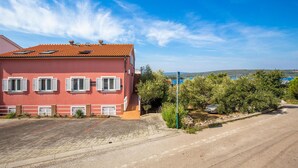A pink building with a tiled roof, a parking sign, and a view of the sea. - 2 bedroom cozy apartment in Punat (Punat)
