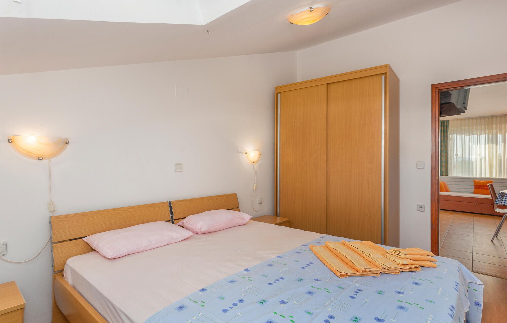 Un dormitorio con cama, armario de madera, lámparas de noche y ventana con vistas.