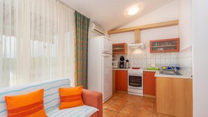 A compact kitchen with a refrigerator, stove, and sink. There's a sofa with orange cushions and a window with sheer curtains. - 2 bedroom cozy apartment in Punat (Punat)