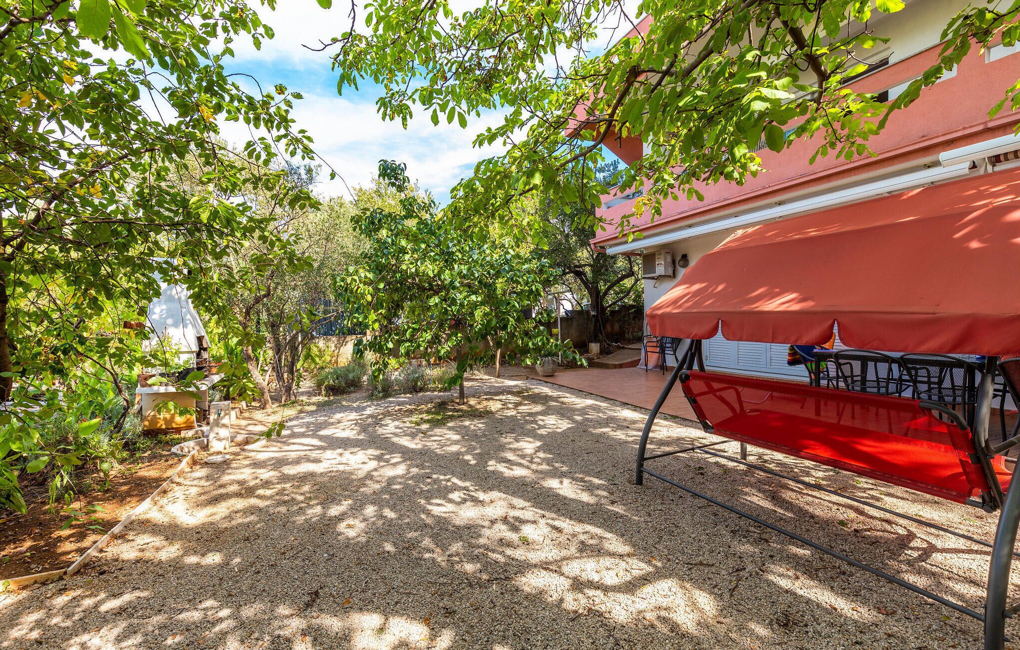 A patio area with a gravel path, a red canopy, and outdoor furniture.