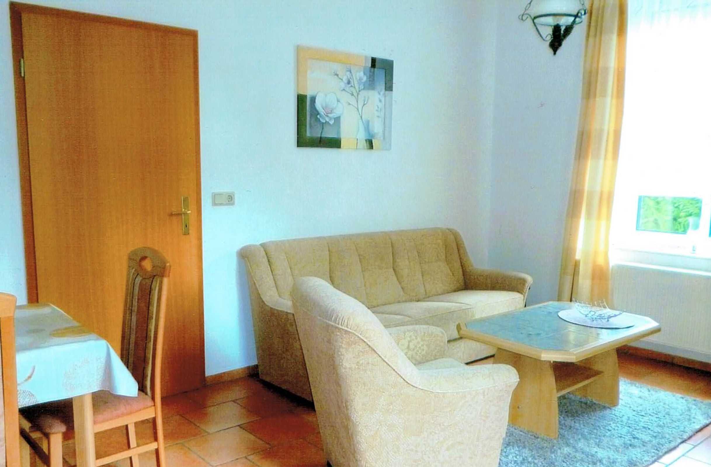 Een kamer met een beige bank, een houten tafel, een houten stoel en een deur.