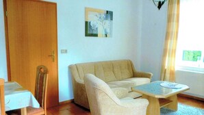 Ein Zimmer mit einem beigefarbenen Sofa, einem Holztisch, einem Holzstuhl und einer Tür.