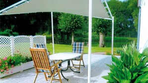 Eine überdachte Terrasse mit Tisch und Stühlen, umgeben von einem weißen Gitterzaun und Pflanzen.