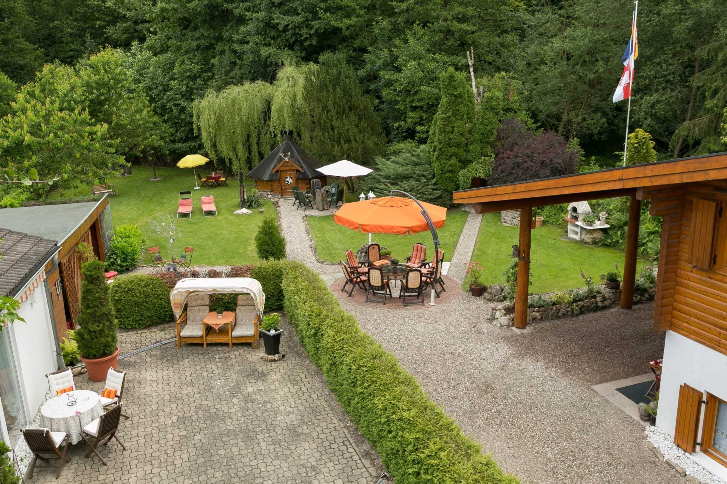 Eine Terrasse mit Tisch und Stühlen, ein kleiner Garten und eine Holzkonstruktion.