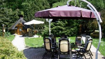 Eine Terrasse mit Tisch und Stühlen, eine Pergola mit Dach und ein Holzhaus im Hintergrund.