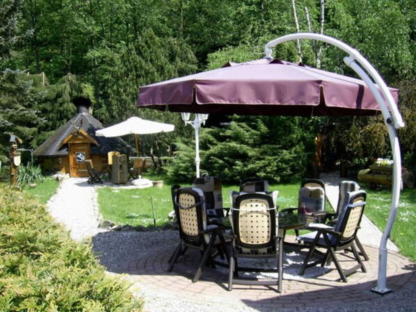 Un patio con mesa y sillas, una pérgola con toldo y una cabaña de madera al fondo.
