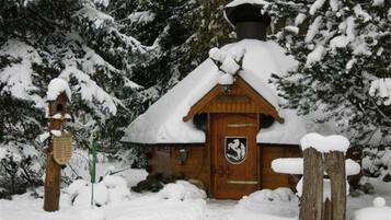Eine Holzhütte mit schneebedecktem Dach, eine Holztür mit Wappen und ein Holzpfosten mit einem Schild.