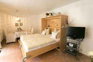 Un dormitorio con cama, mueble para televisión con aparatos electrónicos, mesita de noche y una silla.