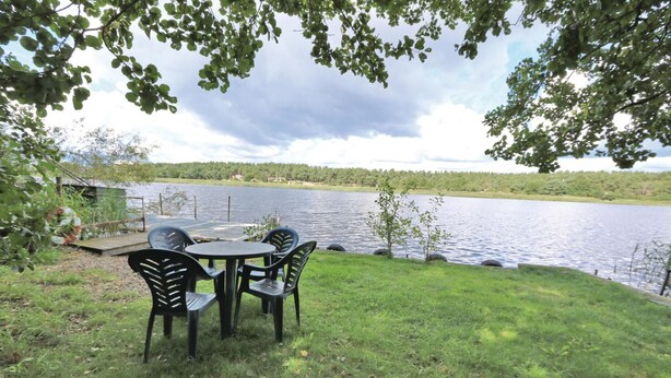 A lakeside outdoor seating area with a table and chairs, surrounded by grass and trees. - 3 bedroom gorgeous home in Yngsjö (Yngsjö)
