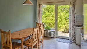A dining area with a wooden table and chairs, a radiator, a window with curtains, and a view of greenery outside. - 3 bedroom gorgeous home in Yngsjö (Yngsjö)