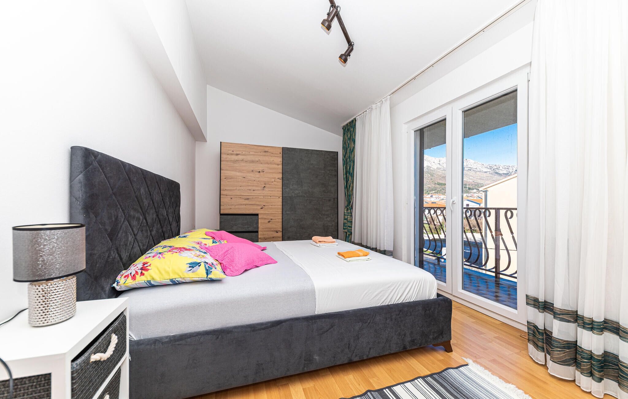 Ein modernes Schlafzimmer mit Bett, Nachttischlampe, Holz-Kopfteil und Blick ins Freie.