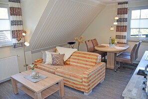 A cozy living room with a striped sofa, a small table, and a dining area with a round table and chairs.