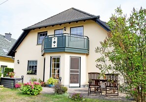 Ein zweistöckiges Haus mit Balkon, Eingangstür und einem kleinen Garten mit Topfpflanzen.