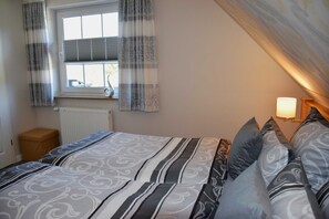 Ein Schlafzimmer mit Bett, Vorhängen, einem Fenster, einem Heizkörper und einer Nachttischlampe.