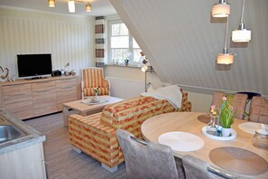 A modern kitchen with a built-in oven, a dining area with a round table and chairs, a sofa, and a television.