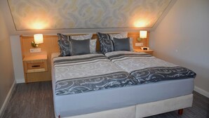 A neatly made bed with patterned bedding, two bedside lamps, a nightstand with a drawer, and a patterned ceiling. - Ferienappartement Garanitzblick - Ferienappartements am Granitzwald (Sellin)