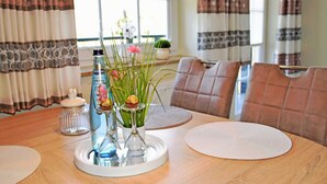 A dining table with a glass vase containing flowers, a bottle of Cristalina water, and a decorative nut. There are placemats and a white plate on the table. - Ferienappartement Garanitzblick - Ferienappartements am Granitzwald (Sellin)