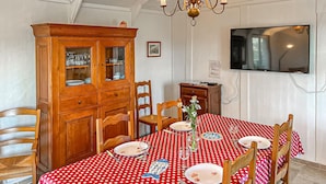 Un comedor con mantel rojo de lunares, sillas de madera, un armario con puertas de vidrio y un televisor montado en la pared.