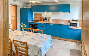 A kitchen with blue cabinets, a wooden table with a fish-patterned tablecloth, and a microwave. - Cozy home in Lestre with WiFi (Lestre)