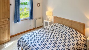 Un dormitorio con cama, ventana con cortinas, lámpara de noche y radiador.