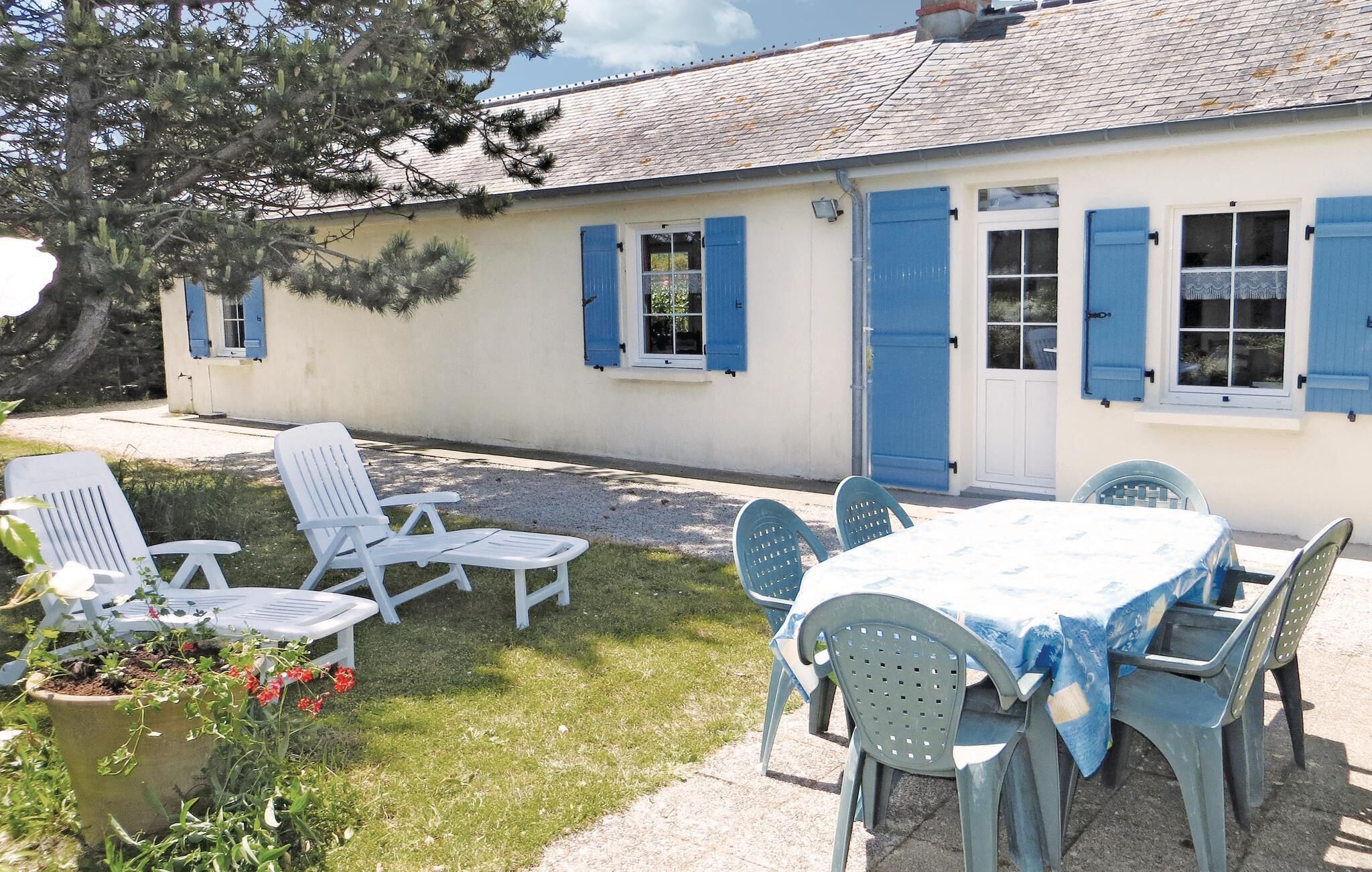 Une maison dotée d’un patio comprenant une table et des chaises, d’un petit jardin avec une plante en pot et d’une porte bleue.
