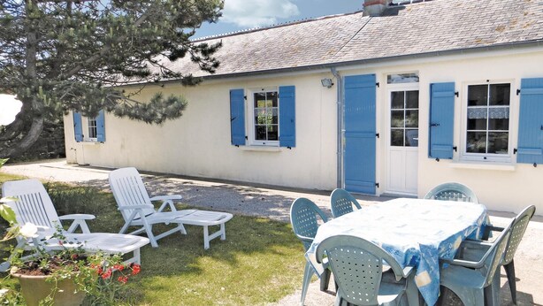 Una casa con un patio que tiene una mesa y sillas, un pequeño jardín con una planta en maceta y una puerta azul.