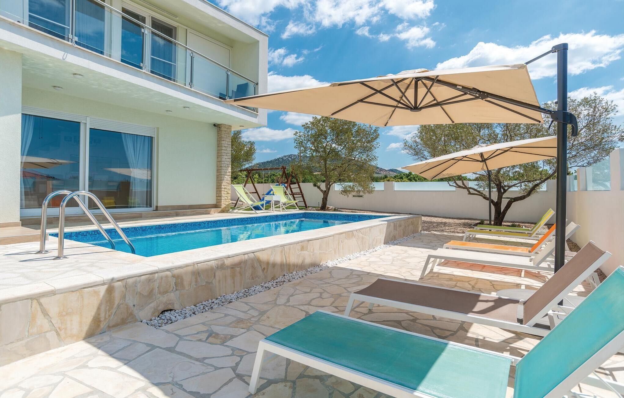 A modern outdoor pool area with a clear blue pool, stone flooring, and lounge chairs.