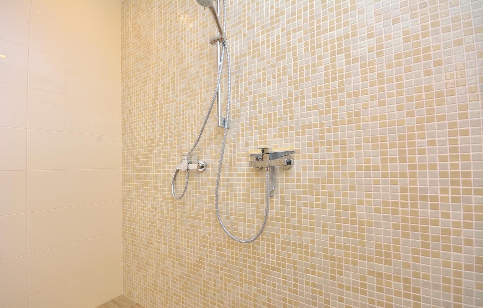 A shower with a tiled wall and a handheld showerhead.
