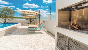 Zona de piscina con un deck de baldosas de piedra, sillones de descanso y una chimenea.