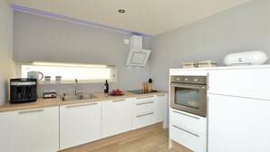 Una cocina moderna con armarios blancos, horno empotrado, cafetera y una ventana sobre el fregadero.