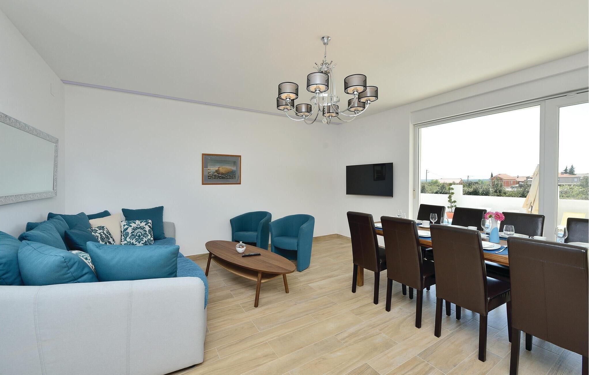 A modern living room with a sofa, chairs, a dining table, and a chandelier.