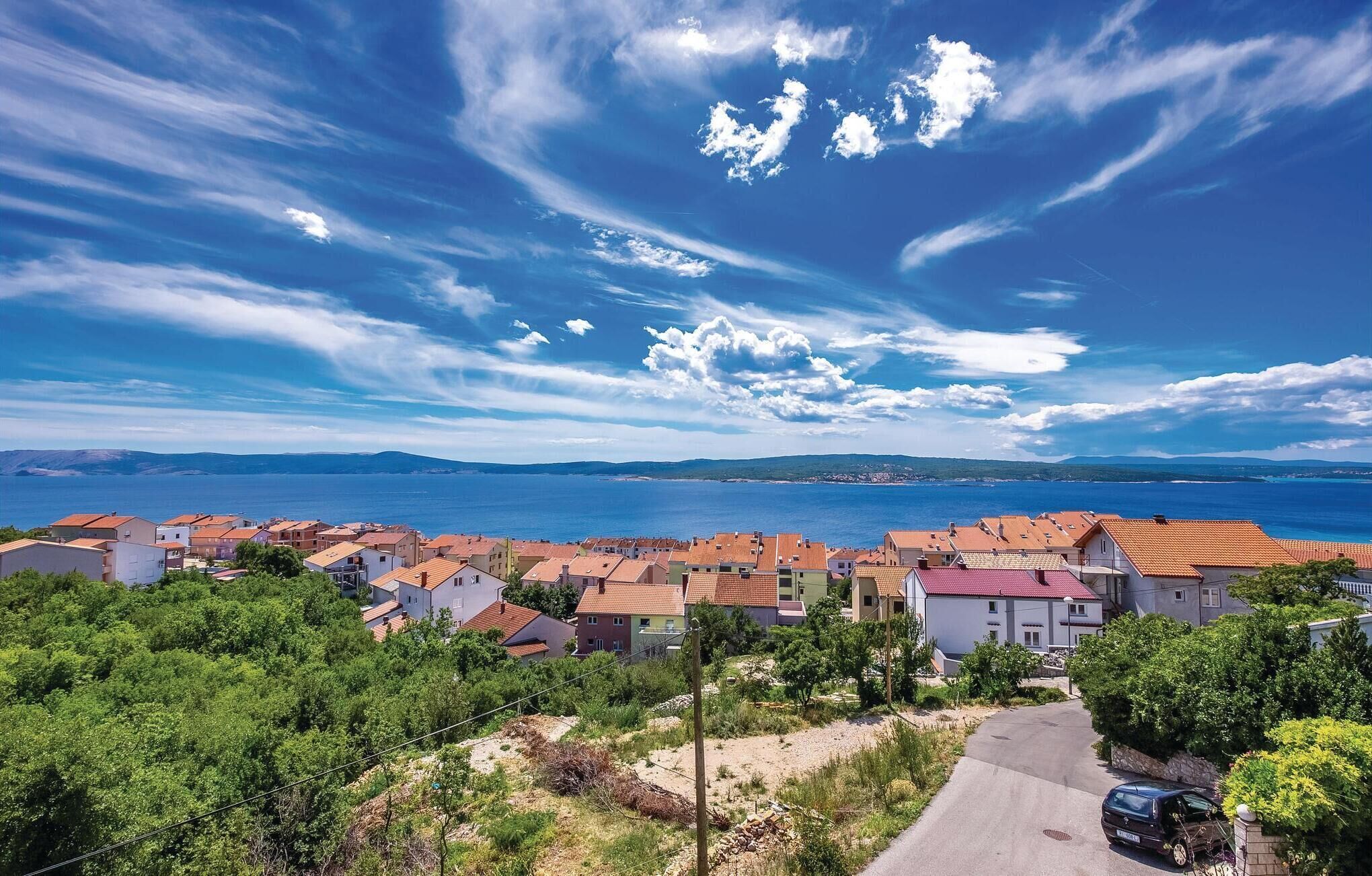 Une ville côtière aux bâtiments aux toits de tuiles rouges, avec un ciel dégagé et une vue sur la mer.