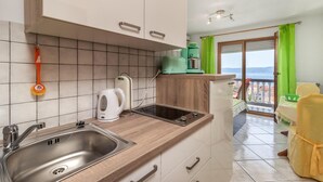 Una cocina moderna con un lavamanos de acero inoxidable, un hervidor, un tostador y una cafetera. Hay un balcón con vistas al mar.