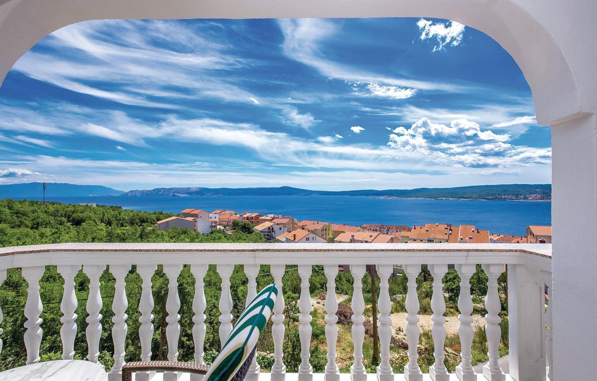A balcony with a view of a coastal town, a clear sky, and distant mountains.