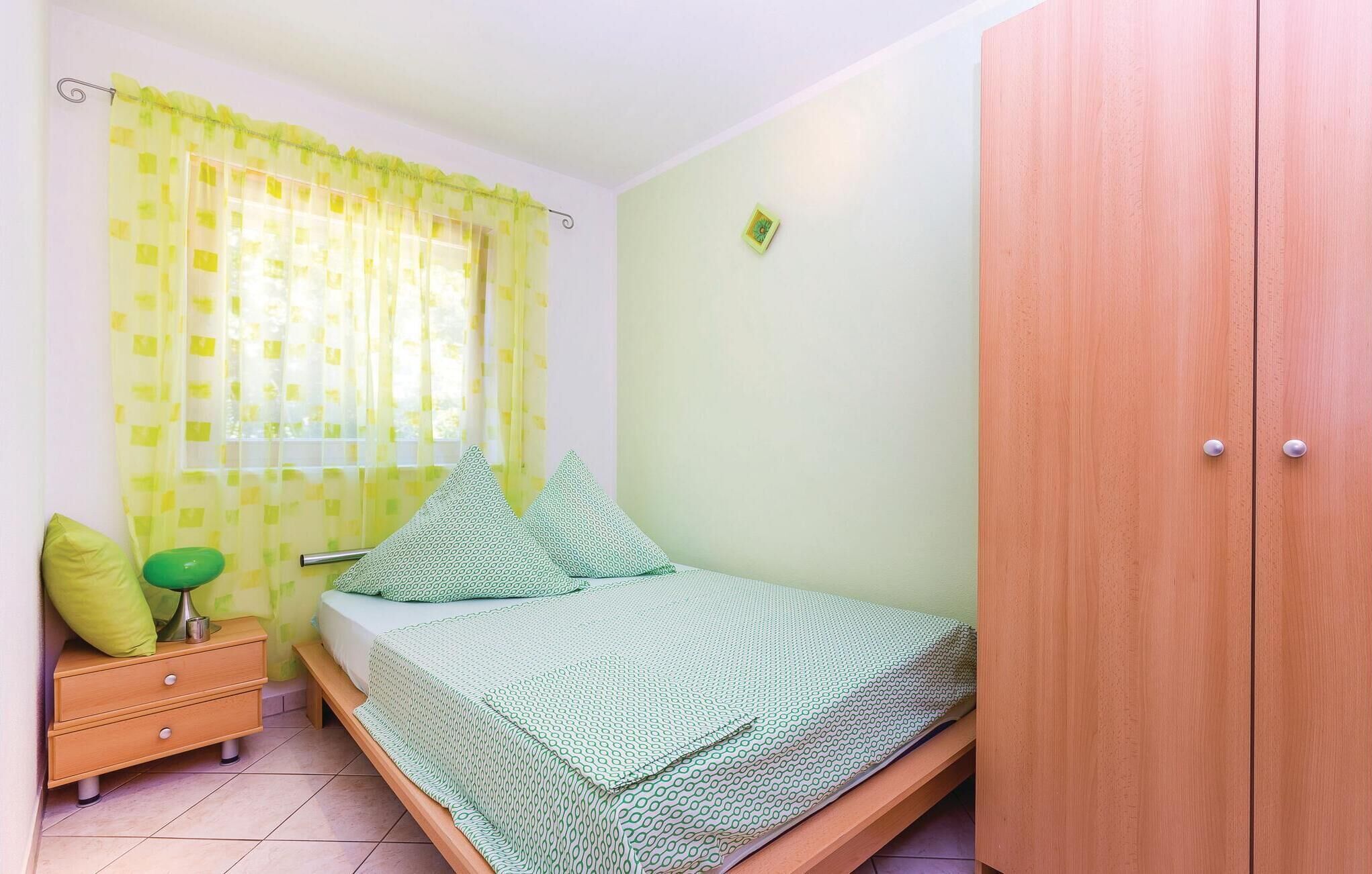 Habitació petita amb un llit individual, un armari de fusta, una taula de nit amb una làmpada i una finestra amb cortines grogues.