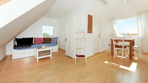 Un dormitorio estilo loft con techo inclinado, un banco empotrado con cojines, un armario blanco, una mesita y una ventana con cortinas.
