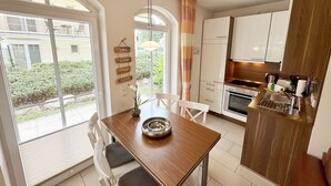Een moderne keuken met witte kasten, een ingebouwde oven en een eethoek met een houten tafel en stoelen.