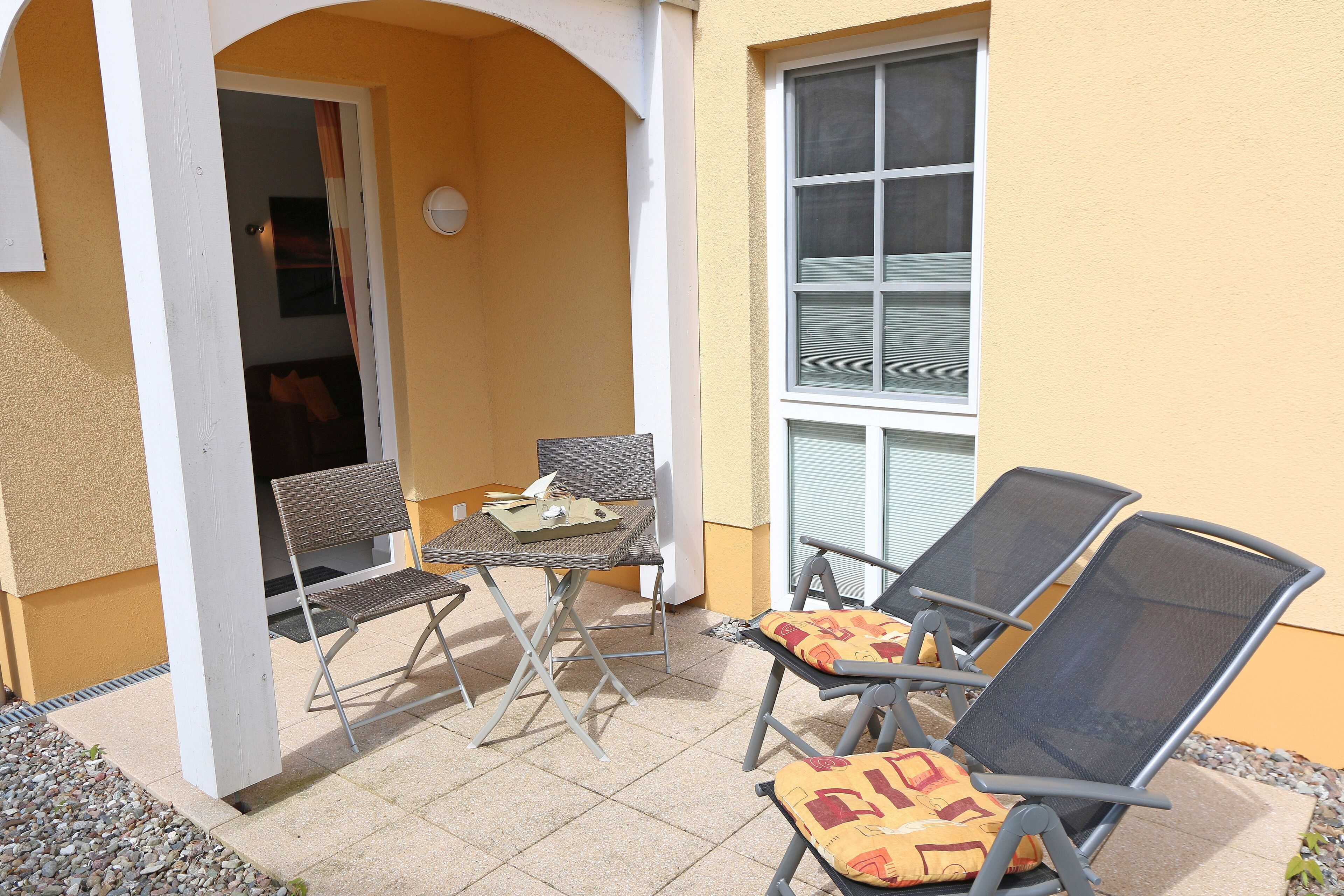 An outdoor seating area with two chairs and a table, a door leading to an interior space, and a window with blinds.