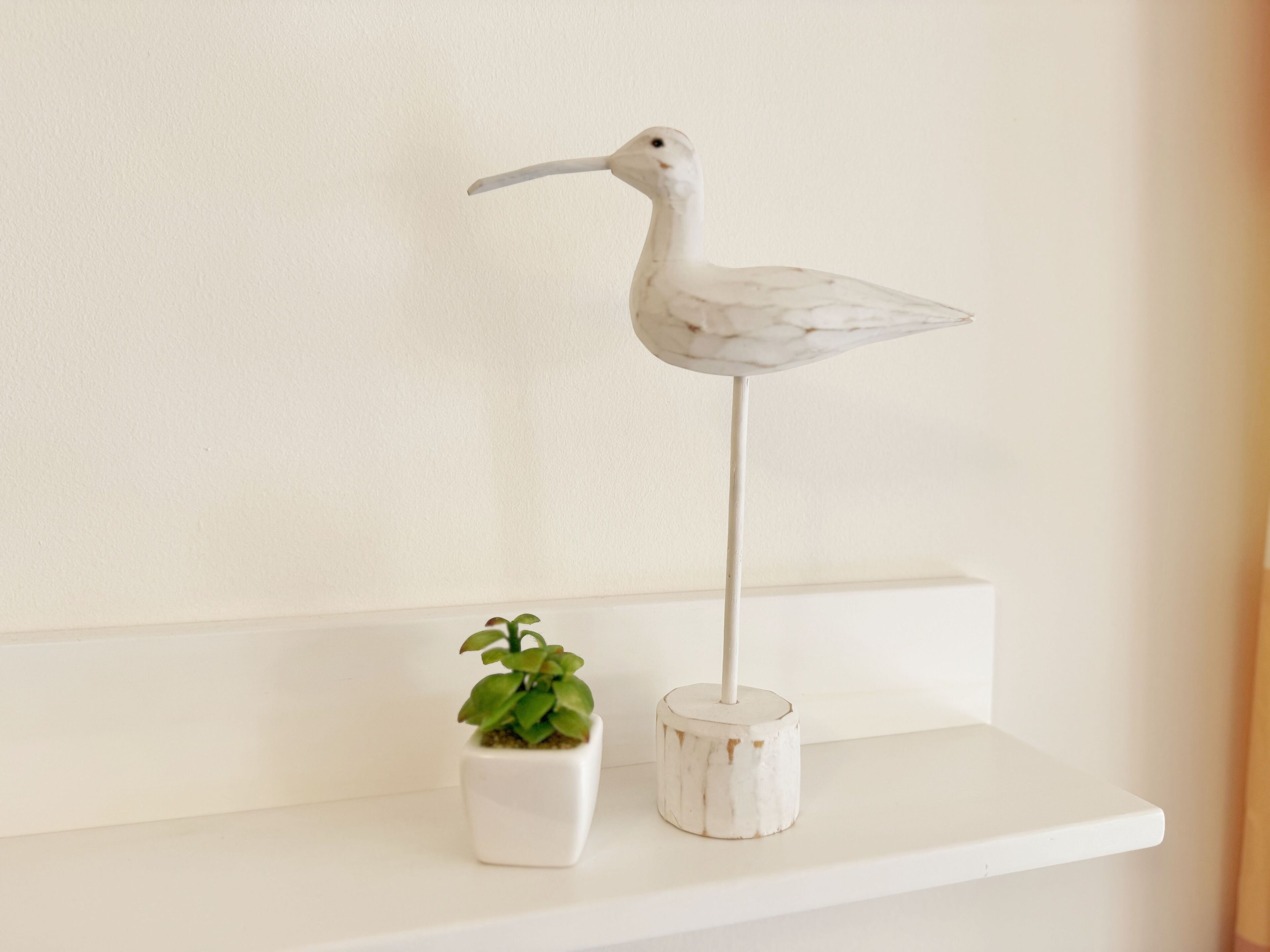 A white shelf with a white bird sculpture and a small potted plant.