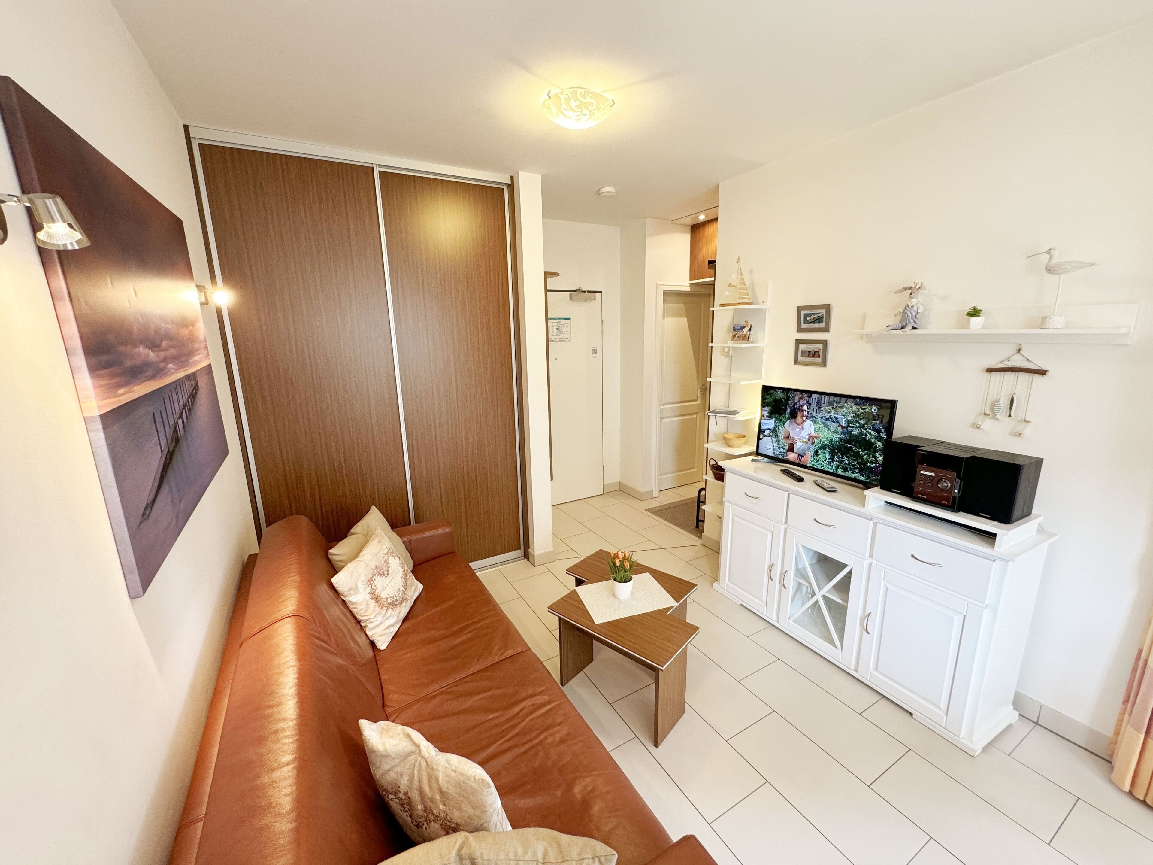 Een moderne woonkamer met een bruine leren bank, een salontafel, een televisie en een wit kastje.