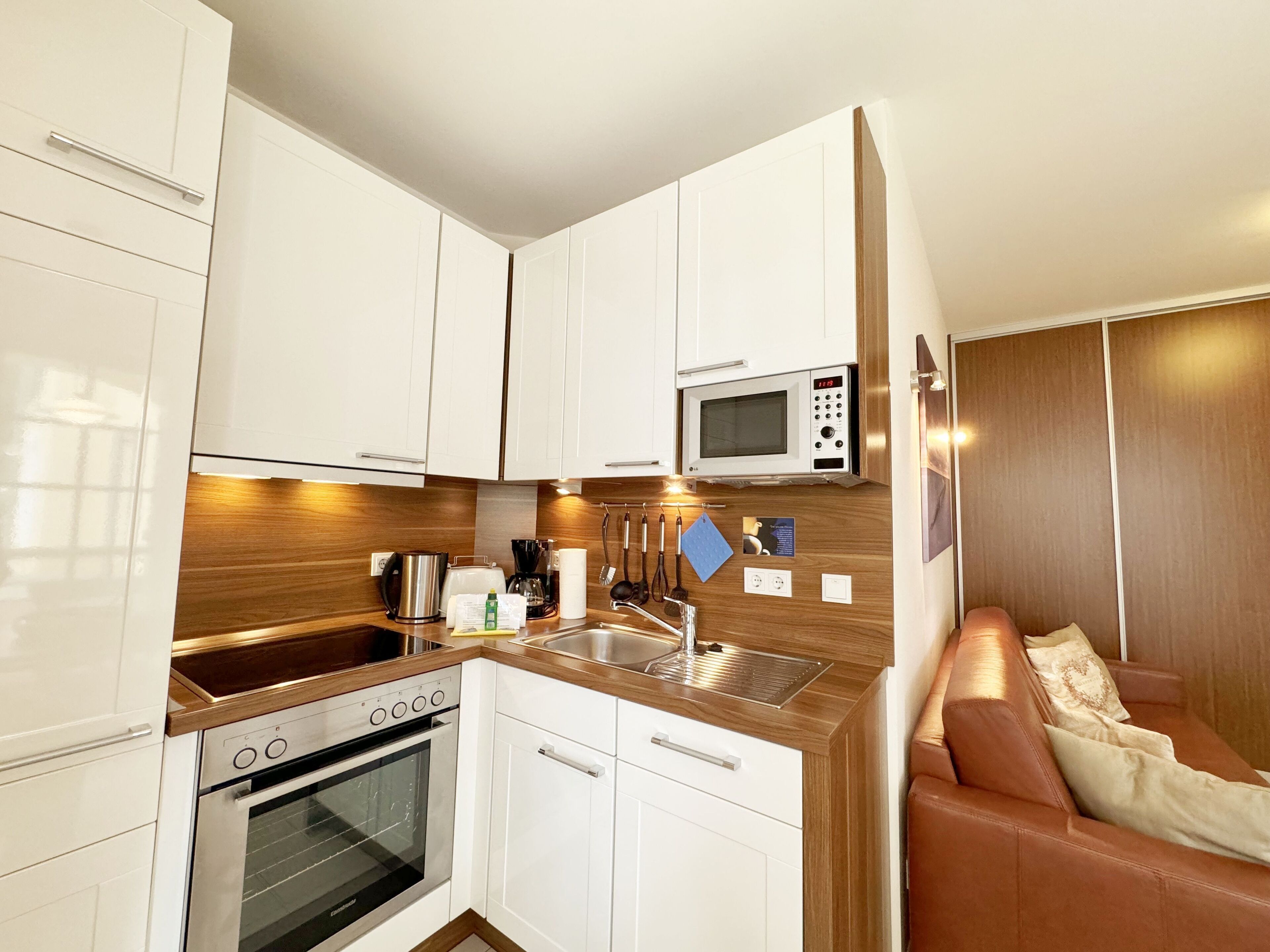 Una cocina compacta con gabinetes blancos, microondas, cafetera y estufa.