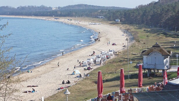 Een strand met tenten en parasols, een waterpartij en een heuvel met bomen.