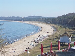 A beach with tents and umbrellas, a water body, and a hill with trees.